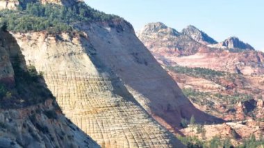 Hava İzleme Çekimi: Zion Ulusal Parkı ikonik kırmızı ve krem rengi kaya oluşumlarının engebeli güzelliğini tecrübe edin. Gün ortası ışıklarıyla yakalanan bu manzara, parkın göz kamaştırıcı doğal manzaralarını vurgular..