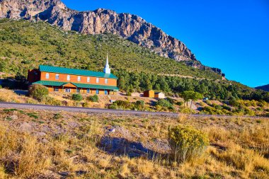 Tranquil rural church with green roof and white steeple stands against Mount Charlestons rugged peaks in Nevada. Golden hour light enhances the serene and spiritual ambiance of this picturesque clipart