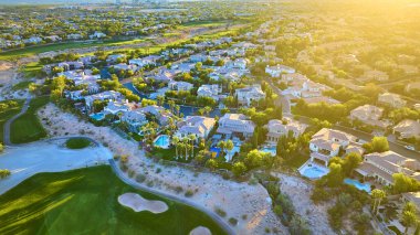 Golden hour over a luxurious Las Vegas suburb, showcasing elegant homes with pools and a golf course, framed by lush greenery against a desert backdrop. Ideal for real estate and lifestyle themes. clipart