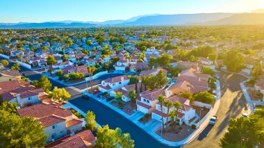 Sakin bir Las Vegas banliyösünün havadan görünüşü: düzenli kırmızı kiremitli evler, yeşil bahçeler, ve altın ışığın altındaki görkemli uzak dağlar. Huzurlu bir yaşam sürmek için mükemmel..