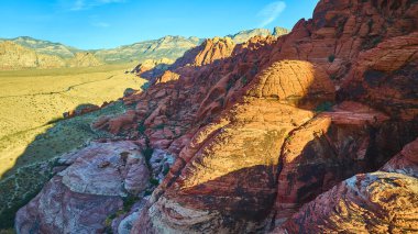 Nevada Red Rock Kanyonu 'nun canlı kumtaşı oluşumlarıyla nefes kesici hava manzarası. Altın bir gökyüzünün altındaki güzelliği deneyimlemek maceracılar ve doğa meraklıları için mükemmeldir..