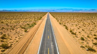 Nevada 'daki Boulder City Kuru Göl Yatağı' nın kurak arazisinden geçen uzun düz bir yolun havadan görünüşü. İzolasyon, özgürlük ve açık yol maceralarının cazibesini tasvir etmek için ideal..