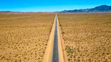 Boulder City Nevada yakınlarındaki ufka uzanan uzun bir çöl otoyolunun havadan görüntüsü. Uçsuz bucaksız mavi gökyüzü altında yalnızlığın ve maceranın özünü yakalamak seyahat ve keşif için mükemmeldir.