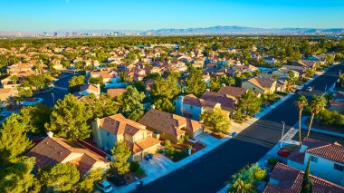 Sıcak öğleden sonra ışığında sakin bir Las Vegas banliyösünün havadan görünüşü, sergilenen terracotta çatıları, palmiye çizgili sokaklar, ve uzak şehir silüeti, emlak ve şehir planlama için ideal.