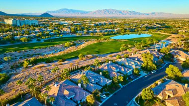Seramik çatılı evleri, yemyeşil golf sahası ve yakındaki kentsel konforları olan lüks bir Las Vegas banliyösünün havadan görünüşü. Sahne altın ışıkta yıkılıyor çarpıcı bir dağ zeminine karşı.