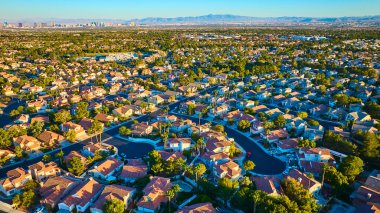 Las Vegas, Nevada 'da sakin bir banliyö mahallesinin hava görüntüsü. Sıcak altın saat ışığı kırmızı kiremitli çatıları ve yeşil ağaçları vurguluyor. Şehir silueti ve uzak dağlar var..