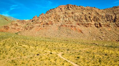 Nevada 'daki Kızıl Kaya Kanyonu' nun havadan görünüşü: açık mavi gökyüzünün altındaki engebeli dağ sıraları. At sırtında yalnız bir binici kurak çölde yürüyor, Amerika 'nın güneybatısında yalnızlığı ve macerayı somutlaştırıyor..