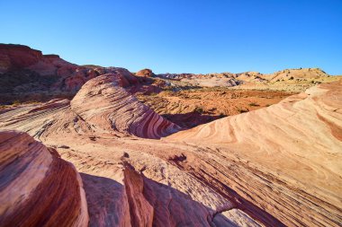 Nevada 'daki Fire State Park Vadisi' nde canlı kaya oluşumları açık mavi gökyüzünün altında dönen kırmızı ve turuncu renkler sergiliyor. Bu çölün nefes kesici yalnızlığını ve jeolojik harikasını tecrübe edin.