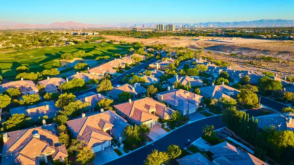 Terracotta çatıları ve yemyeşil çimenleri olan sakin bir Las Vegas banliyösünün havadan görünüşü. Uzaktaki ikonik şehir silueti kontrastı ekler, kentsel yakınlık ve banliyö sükunetinin uyumunu yakalar..