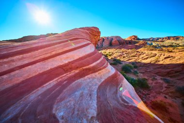 Nevada 'daki Fire State Park Vadisi' nde canlı Ateş Dalgası kaya oluşumu üzerinde gün doğumu. Sersemletici kırmızı, pembe ve beyaz kumtaşı kıvrımları açık mavi gökyüzüne karşı büyüleyici bir doğal görüntü yaratır..