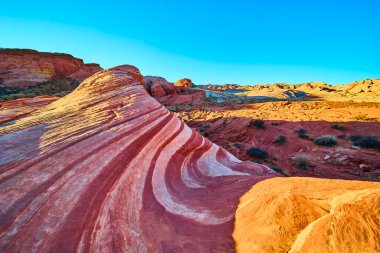 Nevada, Ateş Vadisi 'nde nefes kesen kumtaşı dalgaları, altın saat ışığında parlıyor. Berrak mavi gökyüzünün altındaki bu ikonik çöl manzarasının çarpıcı kıvrımlarını ve canlı renklerini keşfedin..