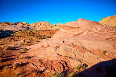 Nevada 'daki Fire State Park Vadisi' nin çarpıcı kırmızı ve turuncu kaya oluşumlarını keşfedin. Altın saat ışığında yıkanan bu çöl manzarası, doğanın sanatını ve jeolojik tarihini gözler önüne seriyor..