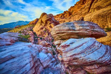 Nevada 'daki Red Rock Kanyonu' nun canlı güzelliğini keşfedin. Büyüleyici bir günbatımında parlayan katmanlı kaya oluşumlarına hayret eden heybetli dağlar ve berrak mavi bir gökyüzü karşısında.