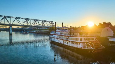 Ohio Nehri boyunca altın saat sükuneti, tarihi Cincinnati nehri teknesi Belle ve sakin bir siluet arkaplanına sahip çelik bir köprü. Seyahat ve eğlence temaları için mükemmel.