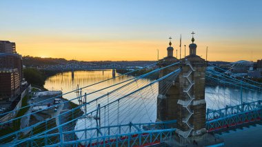 Gün batımında parlayan ikonik John A Roebling Askı Köprüsü 'nün hava görüntüsü. Cincinnati 'yi Ohio Nehri üzerindeki Covington' a bağlıyor. Şehir zarafetini ve sükunetini altın saat ışığında yakalar..