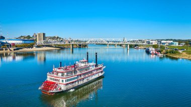 Klasik bir kürek tekeri Cincinnati 'de Ohio Nehri' nde yüzer. Yolcular, canlı bir şehrin ufuk çizgisine karşı nostalji ve kentsel keşifleri harmanlayan modern bir köprü altında manzaralı bir yolculuğun tadını çıkarıyorlar..