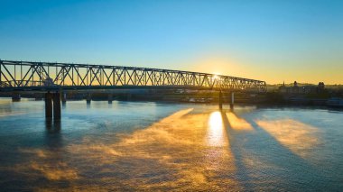 Ohio Nehri üzerindeki altın saat çarpıcı Cincinnati siluetini yakalıyor. Karmaşık endüstriyel köprü, doğanın dingin güzelliğinin ve insan yaratıcılığının bir kanıtı olarak duruyor. Temalar için ideal