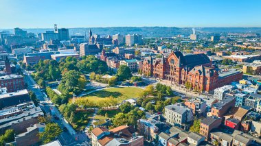 Washington Park 'ın yemyeşil yeşillikleriyle çevrili tarihi kırmızı tuğlalı müzik salonunun güneşli bir günde miras ve modernliği harmanladığı Cincinnati şehir merkezinin havadan görüntüsü..