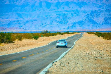 Endless adventure on the open road in Moapa Valley, Nevada. A solitary white car journeys through the stunning Valley of Fire, embraced by majestic mountains and the vast desert landscape.