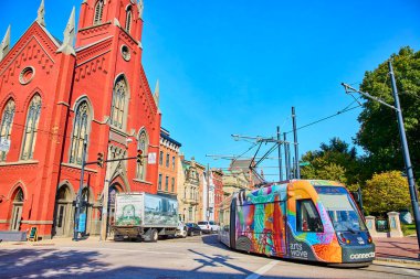 Cincinnati vibrant urban scene featuring a historic red-brick church and a colorful streetcar. A lively blend of tradition and modernity under a clear blue sky. Perfect for depicting city life and clipart