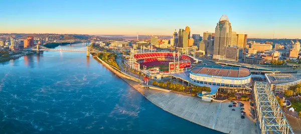 Cincinnati cazibesini yukarıdan keşfedin: Ufuk çizgisi altın saatte ışıldıyor, ikonik John A. Roebling süspansiyon köprüsü ve Great American Ball Park 'ın etrafında hareketli aktiviteler sergiliyor..