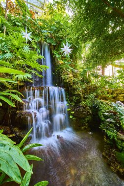 Discover tranquility at Cincinnati lush conservatory. This serene indoor waterfall among vibrant tropical plants creates an exotic escape, perfect for themes of relaxation and nature beauty. clipart