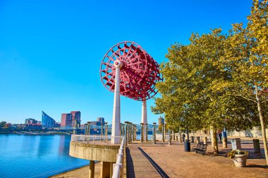 Cincinnati 'deki canlı nehir kenarı sahnesinde mavi gökyüzüne karşı çarpıcı bir kırmızı tekerlek heykeli. Ohio Nehri boyunca modern sanatın ve şehir manzarasının tadını çıkarın. Mükemmel bir kültür ve eğlence karışımı..