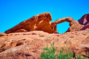 Nevada, Ateş Vadisi 'ndeki görkemli doğal kemer, açık mavi gökyüzüne karşı zaman tarafından oyulmuş kırmızı kumtaşı. Amerikan Güneybatısının hayranlık uyandıran güzelliğini ve engebeli manzarasını tecrübe edin..