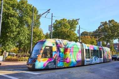 Canlı bir Cincinnati tramvayı, yerel yaratıcılığı teşvik eden renkli sanatlarla süslenmiş, berrak mavi gökyüzünün altındaki ağaçlarla kaplı bir caddede seyahat ediyor, şehirlerin canlı şehir kültürünü somutlaştırıyor..