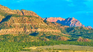 Gooseberry Mesa 'da altın saat parlak bir gökyüzüne karşı görkemli kızıl kaya oluşumlarını gözler önüne seriyor. Aşağıdaki bereketli yeşillik, Utah 'ın nefes kesici ve benzersiz çöl manzarasına zıtlık katıyor..