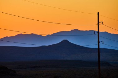 Golden hour over Gooseberry Mesa, Utah: Silhouetted butte and power lines stretch across a vivid sunset, capturing the balance between natures beauty and human innovation in this serene desert clipart