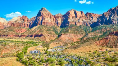 Canlı mavi gökyüzü altında Zion Ulusal Parkı 'nın görkemli kırmızı kaya oluşumlarının havadan görüntüsü. Springdale, Utah aşağıdaki yemyeşil vadi turistlerle dolup taşıyor. Amerika 'da doğa ve macerayı kucaklıyorlar.