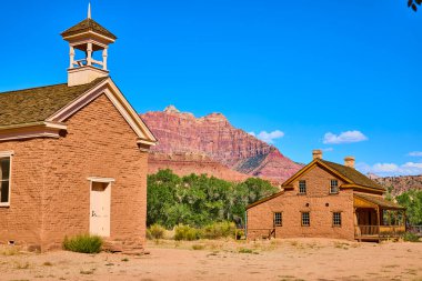 Historic charm meets natural grandeur in Grafton, Utah. Discover the rustic schoolhouse and timeless architecture set against stunning red rock formations under a clear blue sky. A serene escape clipart