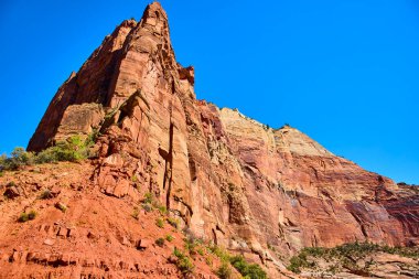 Muhteşem kızıl kaya kayalıkları Utah 'taki Zion Ulusal Parkı' nda gökyüzüne doğru uzanıyor. Canlı kumtaşı katmanları mavi gökyüzüne karşı kontrastlı, Amerikan Güneybatısının engebeli güzelliğini ve macerasını somutlaştırıyor..