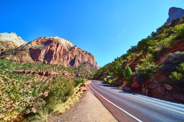 Explore the breathtaking beauty of Zion National Park as a winding road leads you through dramatic red rock mountains and lush greenery under a vibrant blue sky in Springdale Utah. Perfect for clipart