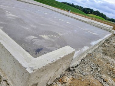 Fort Wayne, Indiana 'da yeni dökülen beton bir temel, doğanın içinde gelişimin ahengini yakalıyor, bulutlu gökyüzünün altında yemyeşil tepeler altında yemyeşil bir zemin olarak yeni başlangıçları simgeliyor..