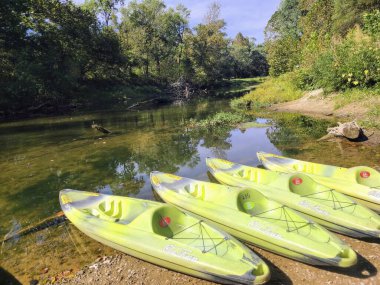 Bright green kayaks await adventure on a peaceful riverside at Hocking Hills, Ohio. Perfect for those seeking tranquility and exploration amidst lush nature and serene waters. Embrace outdoor joy. clipart