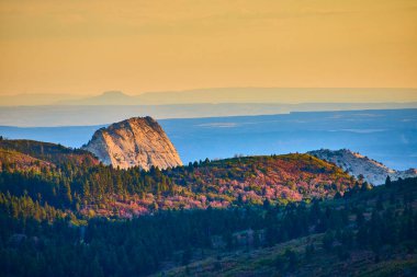 Golden light bathes Kolob Canyon rugged rock formation at Zion National Park, surrounded by autumn hues and misty blue mountains. Experience the serene beauty of natures transition in Utah. clipart