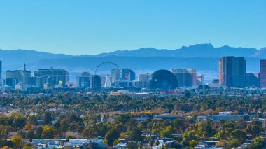 Canlı Las Vegas siluetinin MSG Sphere ve yüksek tekerlekli dönme dolaba sahip ikonik şeritli görüntüsü. Majestic dağları bu hareketli eğlence ve turizm merkezini çerçeveletiyor.