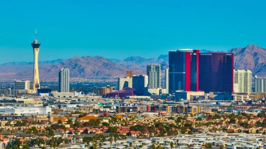 Aerial view of Las Vegas showcasing the Stratosphere Tower against a backdrop of desert mountains. The vibrant skyline features iconic hotels along The Strip under a sunny blue sky. Ideal for travel clipart