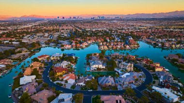 Gün batımında Las Vegas banliyösünün havadan görüntüsü. Virajlı sokaklar ve su yolları sakin bir zemin oluşturuyor, ikonik şehir manzarası ve dağlara zıtlık ekleniyor. Gayrimenkul ve yaşam tarzı temaları için ideal.
