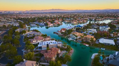 Las Vegas 'ın altın saatinde lüks bir semtinin havadan görünüşü zarif evler, dolambaçlı kanallar ve şehrin ufuk çizgisi. Deneyim dingin, lüks gün batımı yansımalarıyla yaşamak.