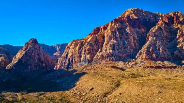 Nevada 'daki Red Rock Kanyonu' nun nefes kesici manzarası. Açık mavi gökyüzü altında parlak kırmızı ve kahverengilerle yükselen kaya oluşumları bu Mojave Çölü manzarasının ham güzelliğini gözler önüne seriyor..