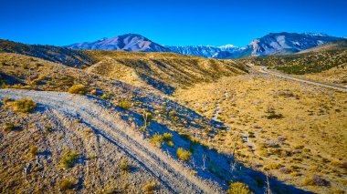 Las Vegas yakınlarındaki uçsuz bucaksız çöl manzarasının hava görüntüsü, uzakta görkemli karla kaplı Charleston Dağı, Nevada 'daki macera ve keşif ruhunu yakalıyor..