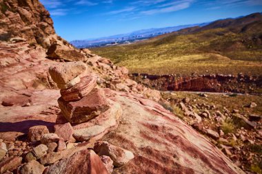 Nevada 'daki Red Rock Canyon' da sakin bir çöl sahnesi. Dengeli kaya yığını canlı manzaraya karşı duruyor, barışı ve doğayla bağlantıyı simgeliyor..