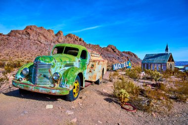 Nelson Nevada 'nın unutulmuş cazibesini keşfedin. Paslı yeşil bir kamyon, açık bir gökyüzünün altında, eğilmiş bir motel tabelasının ve eski bir şapelin yanında, nostalji ve zamanın geçişini anımsatıyor..
