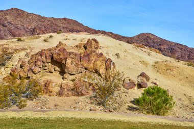 Bask in the rugged beauty of Boulder City, Nevada, where reddish-brown rock formations rise majestically from the arid terrain. Discover a serene desert landscape under a vibrant blue sky. clipart