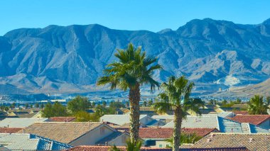 Canlı bir Las Vegas mahallesinin havadan görünüşü dramatik bir dağ zeminine kurulmuştu. Bereketli palmiye ağaçları ve sıcak tonlu çatılar açık mavi çöl gökyüzü ile çarpıcı bir kontrast oluşturur..