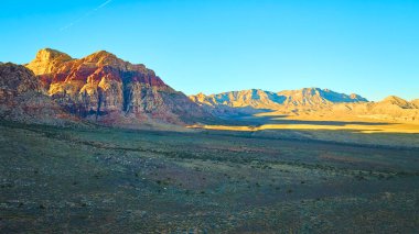 Nevada 'daki Kızıl Kaya Kanyonu' nun nefes kesici güzelliğini tecrübe edin. Altın saat güneşi canlı kayalıkları aydınlatıyor ve sakin çöl manzarası boyunca uzun gölgeler bırakıyor. Doğa için mükemmel.