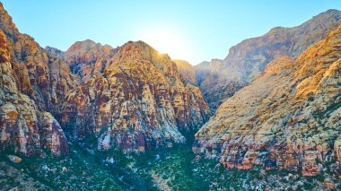 Gün doğumunda Nevada 'daki Lost Creek Kanyonu' nun havadan görüntüsü. Güneş ışığı, aşağıdaki kızıl kayalıkları ve yemyeşil vadiyi yıkıyor ve Las Vegas yakınlarındaki çöl manzarasının dingin güzelliğini yakalıyor. Tam oldu.